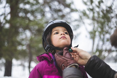 Mature man helping daughter wearing helmet during winter