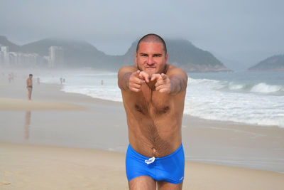 Happy shirtless man gesturing at beach