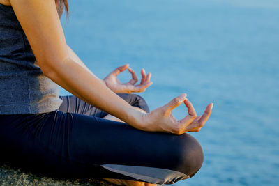 Midsection of woman practicing yoga at beach