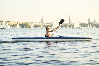 Side view of mid adult woman canoeing on sea against clear sky during sunset