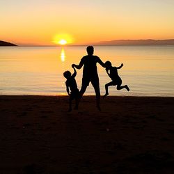 Silhouette children playing on beach against sea during sunset