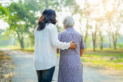 Rear view of woman helping disabled female with mobility walker on road