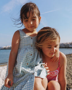 Portrait of sisters sitting  at beach and looking away