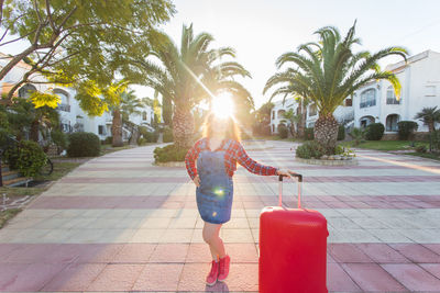 Woman standing by palm trees on footpath