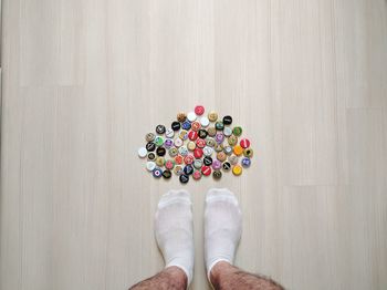 Low section of man wearing socks while standing by various bottle caps on hardwood floor