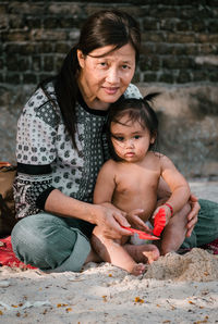 Portrait of smiling mature woman with granddaughter sitting on beach