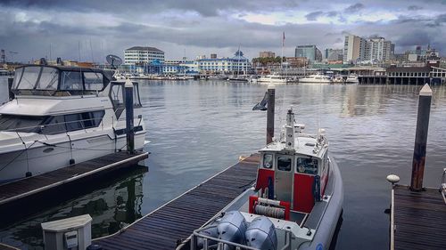 Boats moored at harbor in city against sky