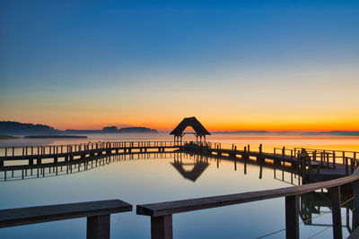 Silhouette swimming pool by sea against sky during sunset