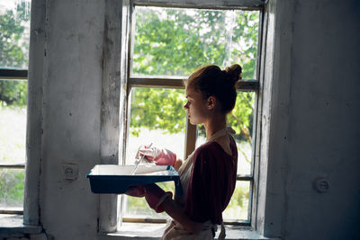 Rear view of young woman standing by window