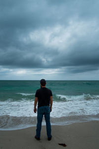 Rear view of man standing on beach against sky