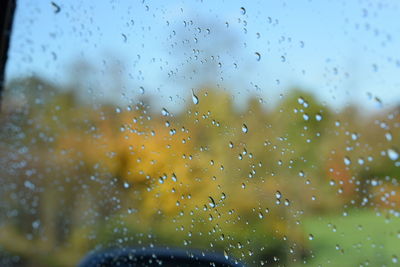 Close-up of water drops on window against sky