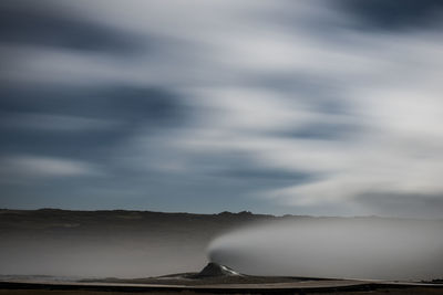 Scenic view of volcano erupting steam against cloudy sky