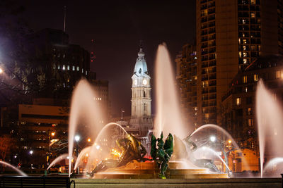 Illuminated fountain against buildings at night