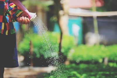 Midsection of woman watering plants at yard