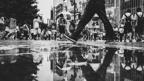 People reflecting in puddle on city street during rainy season