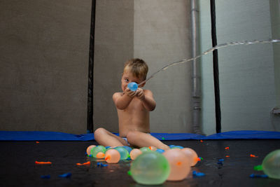 Shirtless boy splashing water from balloon at home
