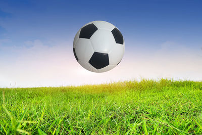 Digital composite image of soccer ball over field against blue sky