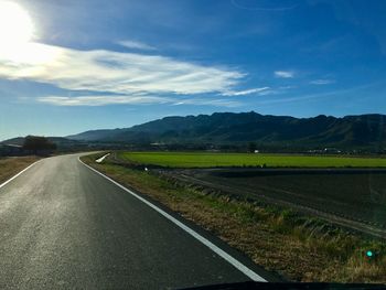 Empty road by field against sky