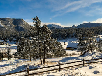 Winter landscape with mountains, trees, split rail fence, blue sky and a construction site