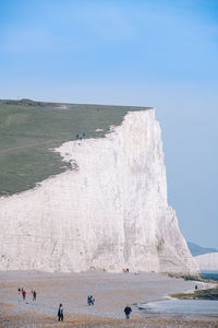 People at beach against cliff and sky