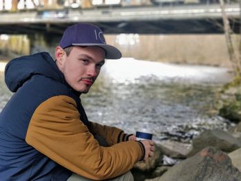 Portrait of young man sitting at riverbank