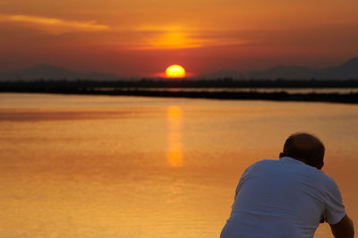 Rear view of man against orange sky during sunset