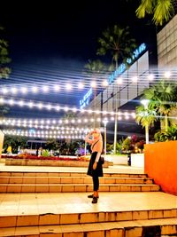 Rear view of man walking on illuminated footpath at night