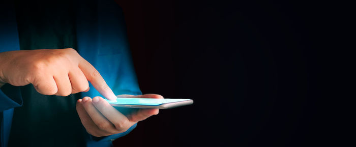 Midsection of man holding smart phone against black background