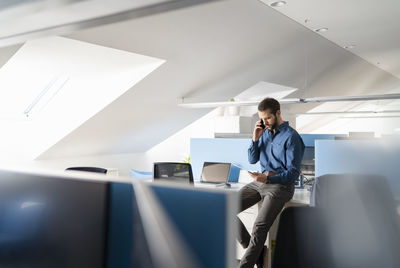 Young businessman using digital tablet while talking on mobile phone at office