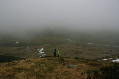 Rear view of father and son standing on field during foggy weather