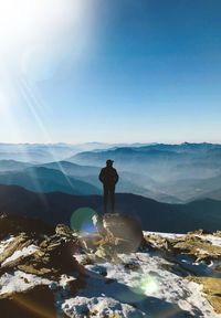 Rear view of silhouette man standing on mountain against sky during sunny day