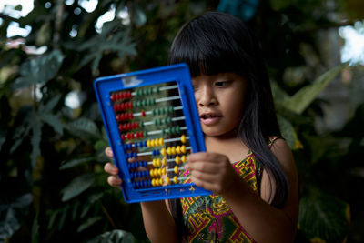 Close-up of girl playing with abacus against plants