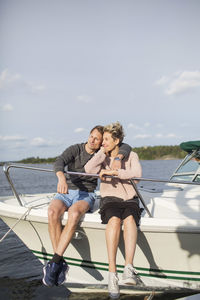 Loving couple sitting on yacht against sky