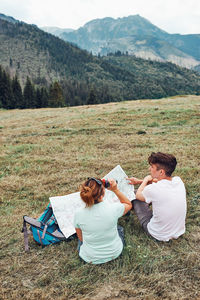 Family examining a map of mountains trials sitting on grass enjoying summer day during vacation trip