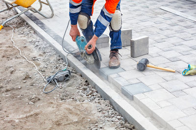 A construction worker evenly cuts paving slabs with a grinder when paving a sidewalk.