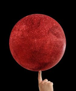 Close-up of hand holding red moon against black background