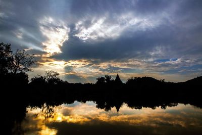 Reflection of silhouette trees on landscape against sky