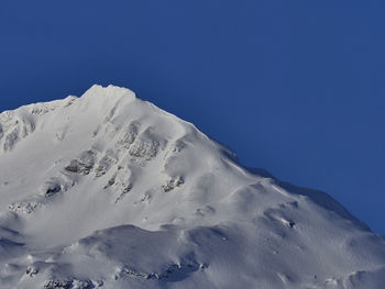 Low angle view of snowcapped mountain against clear blue sky