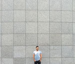 Happy man standing with hands in pockets against wall