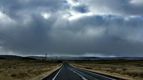 Road passing through field against cloudy sky