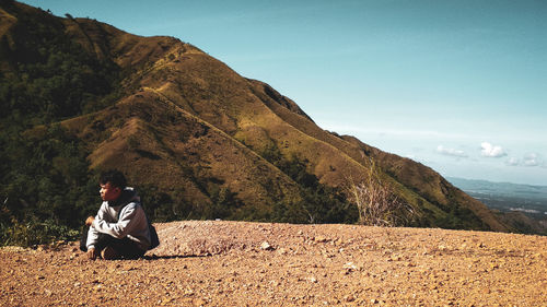 Man sitting on field against mountain