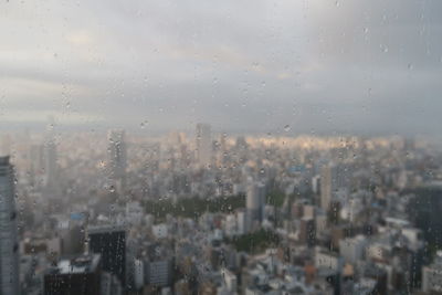 City against sky seen through wet glass window