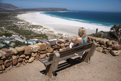 Rear view of woman sitting on beach against sky