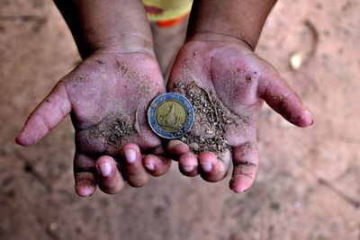 Cropped dirty hands of child holding coin outdoors