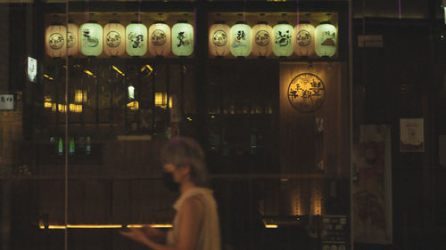 Side view of woman standing in illuminated restaurant at night
