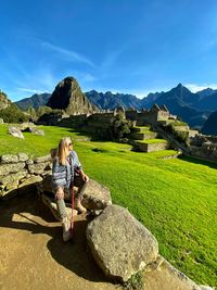 Full length of woman sitting on rock at machu picchu against blue sky