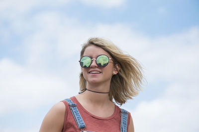 Portrait of smiling young woman wearing sunglasses against sky