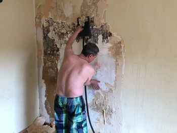 Shirtless man working on weathered wall