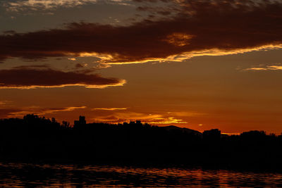 Silhouette trees by sea against orange sky