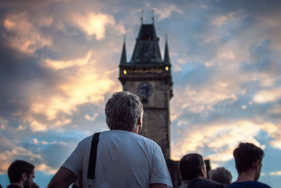 Rear view of people by astronomical clock tower against cloudy sky during sunset